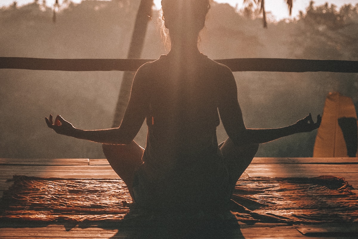Silhouette of a person sitting in lotus position, meditating backlit at sunrise