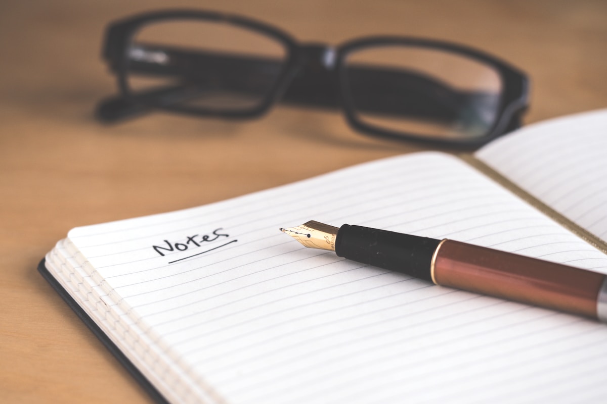 An open notebook with the word "Notes" handwritten, a fountain pen and glasses beside it